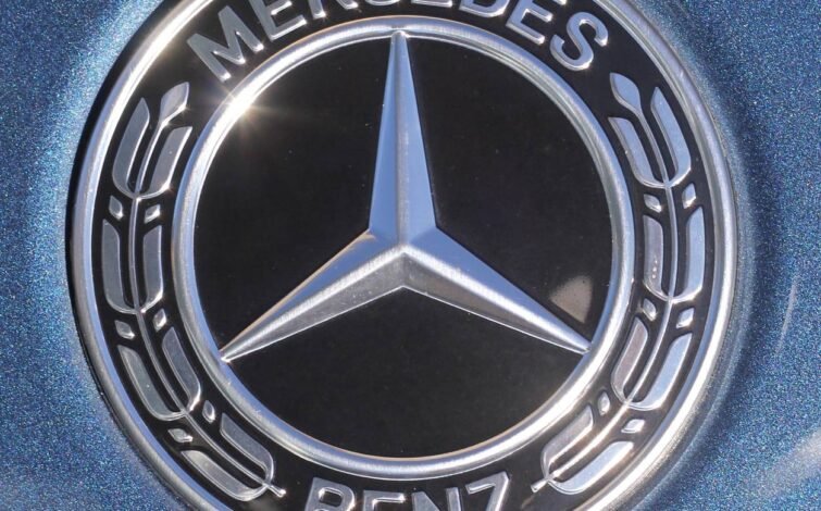 Primer plano del emblema clásico de Mercedes-Benz en el maletero del coche, sobre una pintura metálica azul.