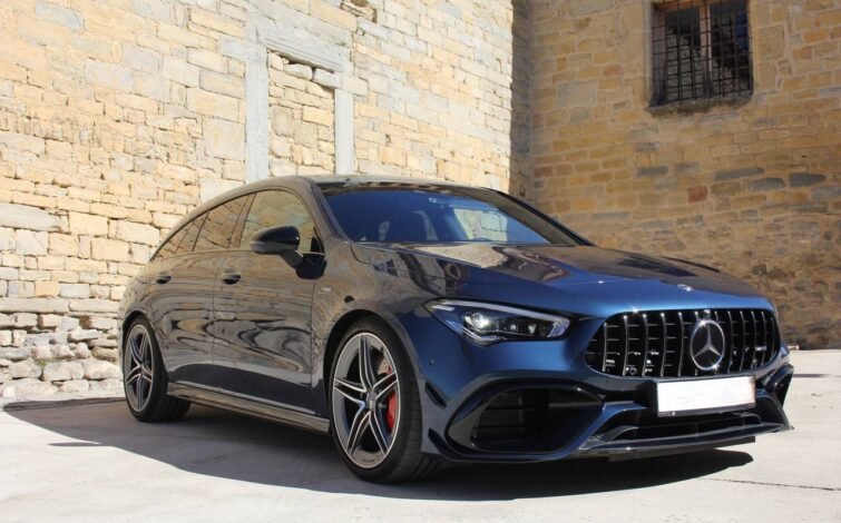 Vista frontal lateral izquierda del Mercedes-Benz CLA 45 S AMG 4MATIC+ azul estacionado frente a una pared de piedra, destacando sus llantas AMG, pinzas de freno rojas y diseño aerodinámico.