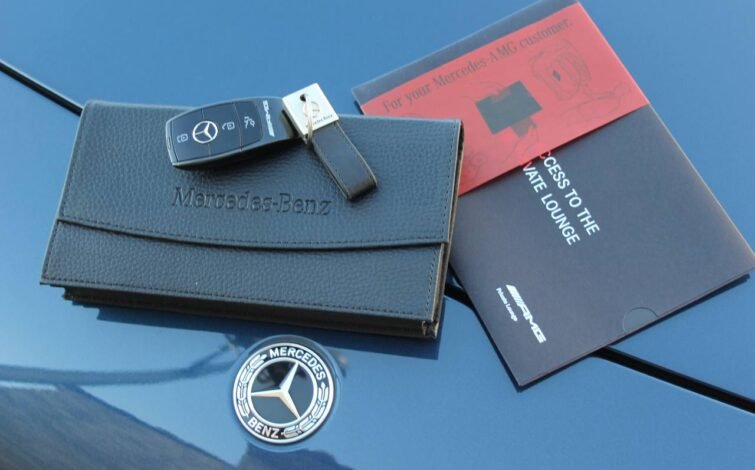 Estuche de cuero con el logotipo Mercedes-Benz, junto con una llave inteligente AMG y folleto de bienvenida sobre el capó del coche.
