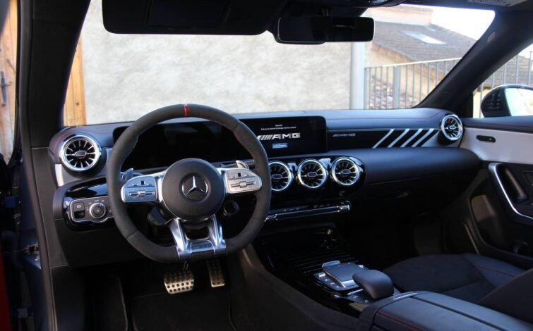 Interior del Mercedes-AMG CLA 45 S con vista al volante deportivo, panel de instrumentos digital y salidas de aire tipo turbina, destacando detalles en aluminio y costuras rojas.
