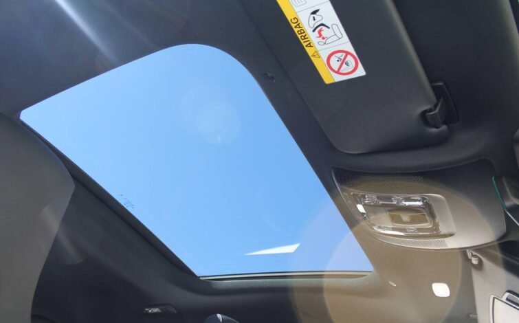 Vista desde el interior hacia el techo panorámico del CLA 45 S, mostrando el cielo azul a través del cristal y parte del parasol con advertencias de airbag.